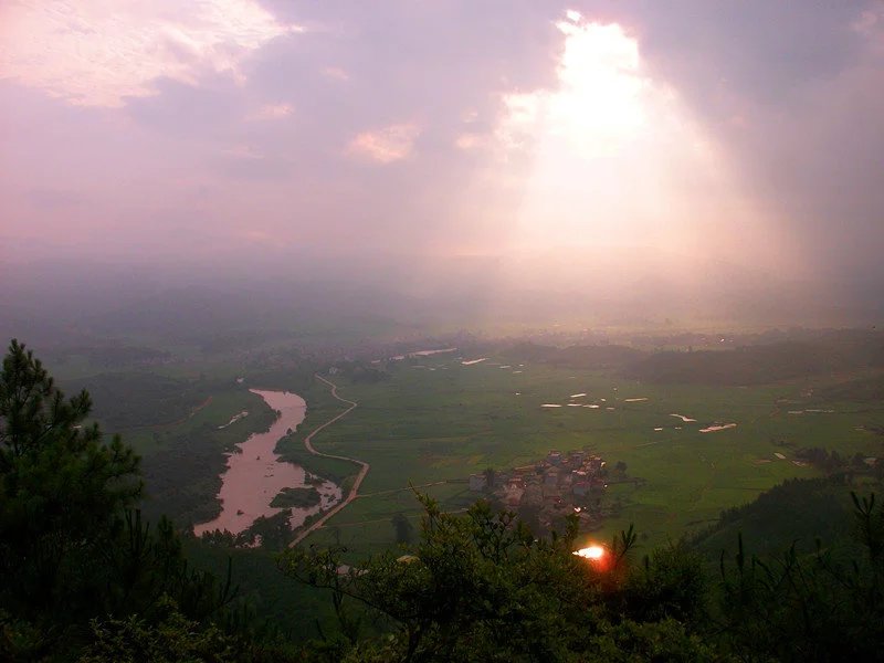 乌黑压天，突然一束光从云层穿出，照在田园中央的小村上，此景非常难得．